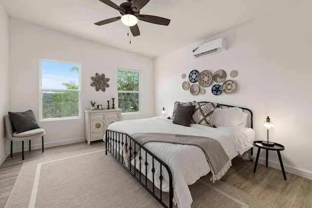 bedroom with wood finished floors, baseboards, a wall mounted air conditioner, and ceiling fan