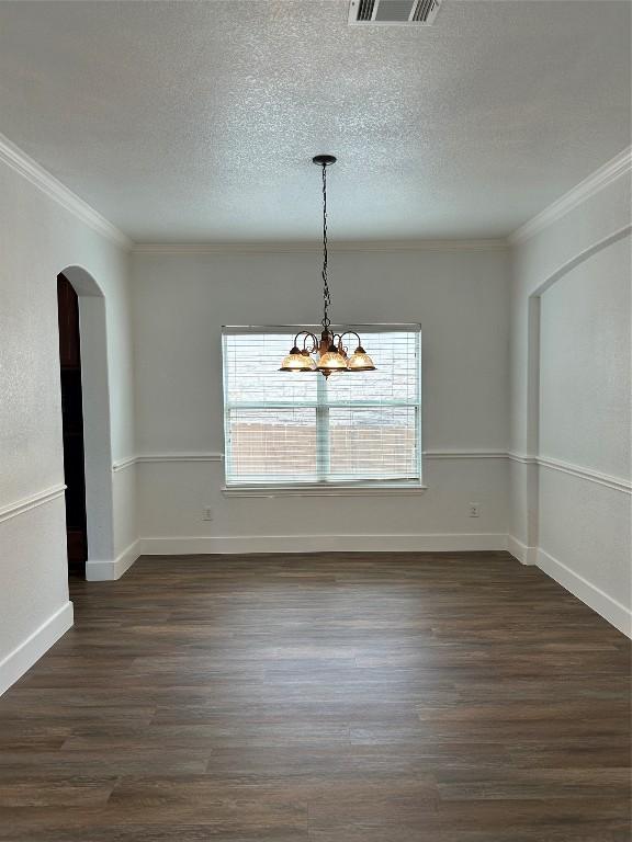 unfurnished dining area featuring an inviting chandelier, ornamental molding, and dark hardwood / wood-style flooring