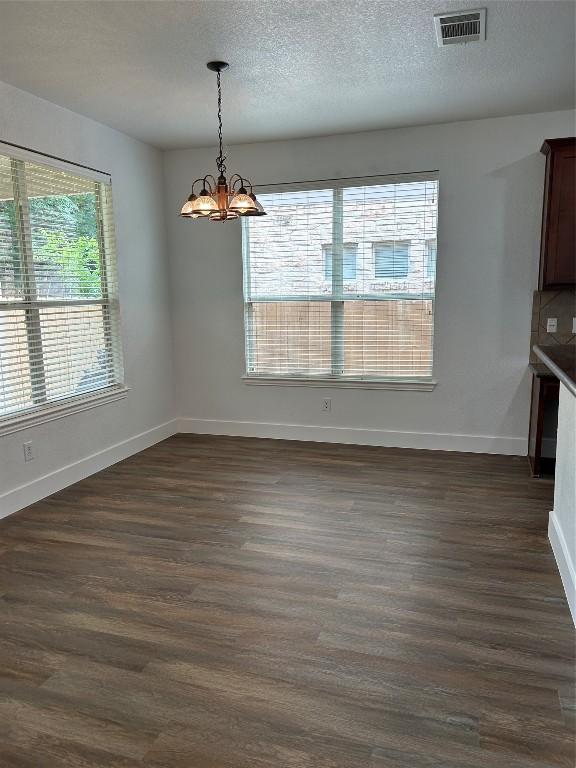 unfurnished dining area with a healthy amount of sunlight, a textured ceiling, a notable chandelier, and dark hardwood / wood-style floors