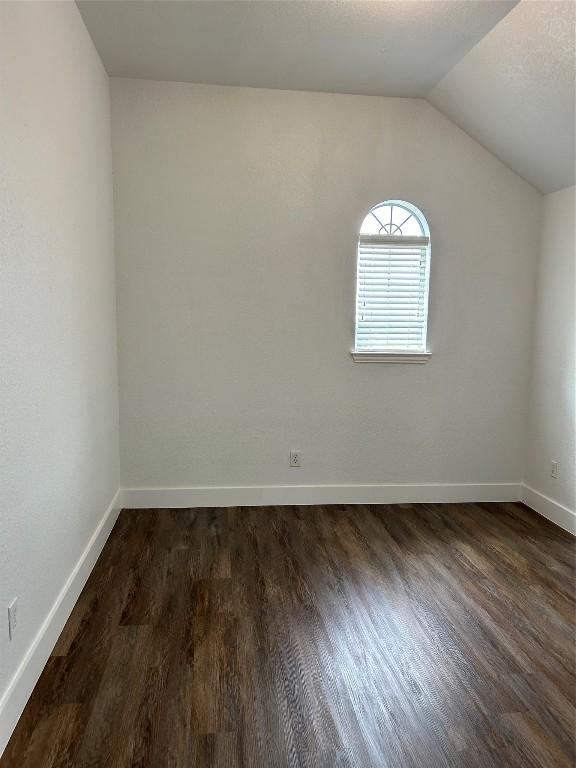 unfurnished room with vaulted ceiling and dark wood-type flooring