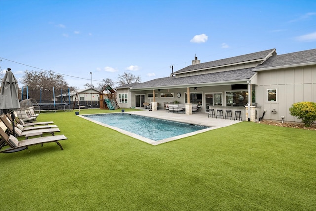 back of house with an outdoor bar, a playground, a lawn, a trampoline, and a patio