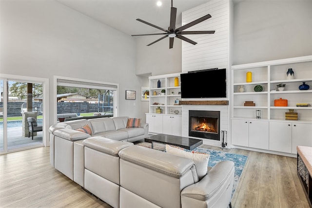 living room featuring a high ceiling, a large fireplace, light wood-type flooring, and a healthy amount of sunlight