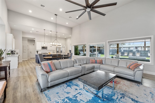 living room with light wood-type flooring, ceiling fan, and a high ceiling