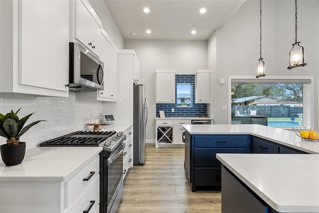 kitchen with hanging light fixtures, appliances with stainless steel finishes, white cabinetry, blue cabinets, and a kitchen island