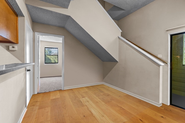 additional living space featuring vaulted ceiling, light hardwood / wood-style floors, and a textured ceiling