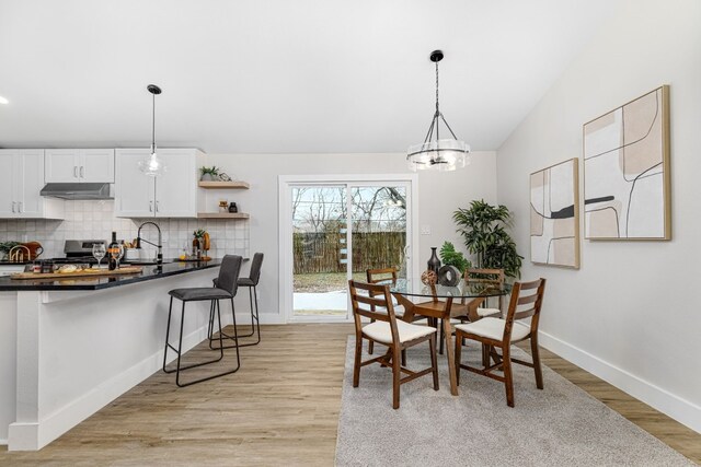 dining area with vaulted ceiling, sink, an inviting chandelier, and light hardwood / wood-style flooring