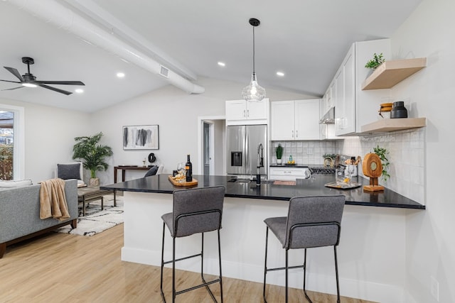 kitchen featuring stainless steel fridge, light hardwood / wood-style floors, white cabinets, a kitchen bar, and kitchen peninsula