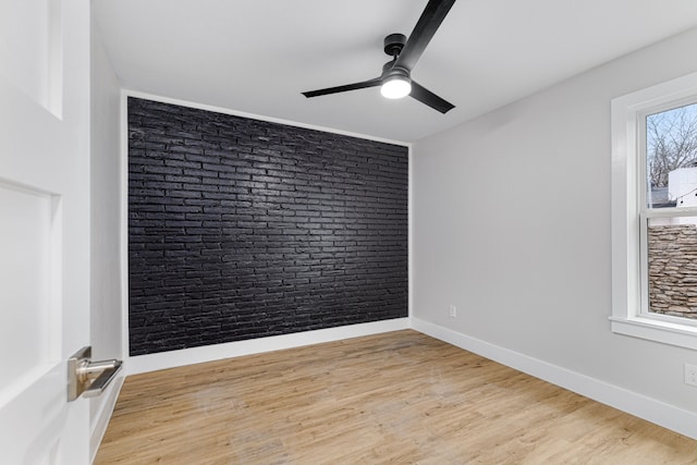 empty room with light wood-type flooring, ceiling fan, and brick wall