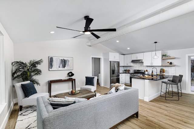 living room with ceiling fan, sink, lofted ceiling with beams, and light hardwood / wood-style flooring