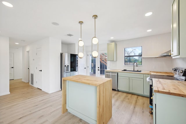 kitchen with stainless steel appliances, a center island, hanging light fixtures, and wood counters