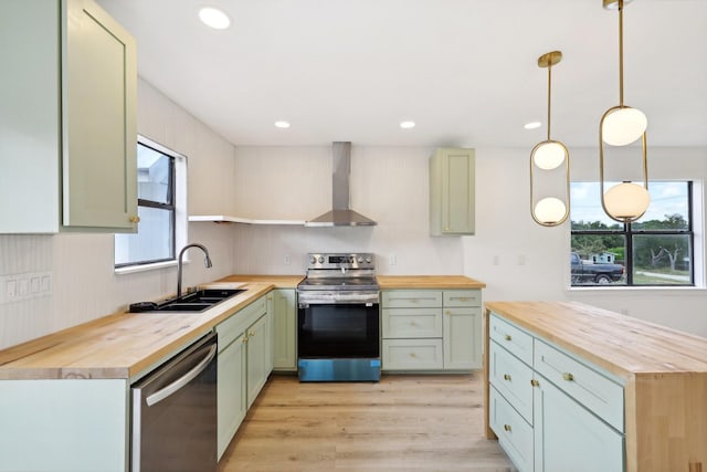 kitchen with appliances with stainless steel finishes, wall chimney exhaust hood, sink, decorative light fixtures, and wooden counters