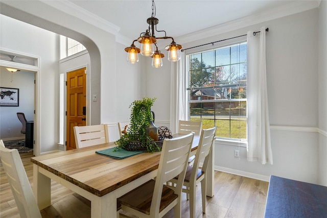 dining room with arched walkways, a notable chandelier, baseboards, ornamental molding, and light wood finished floors