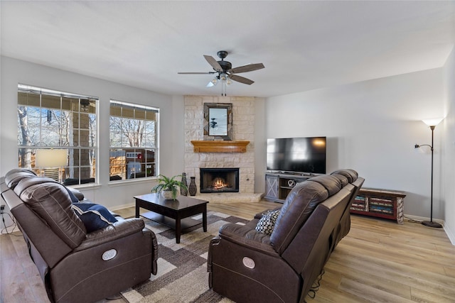 living room with a stone fireplace, light hardwood / wood-style flooring, and ceiling fan