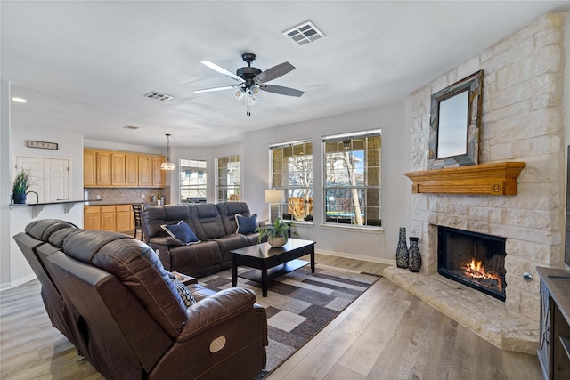 living room featuring ceiling fan, a stone fireplace, and light wood-type flooring