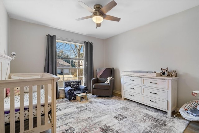 bedroom featuring ceiling fan, a crib, and baseboards