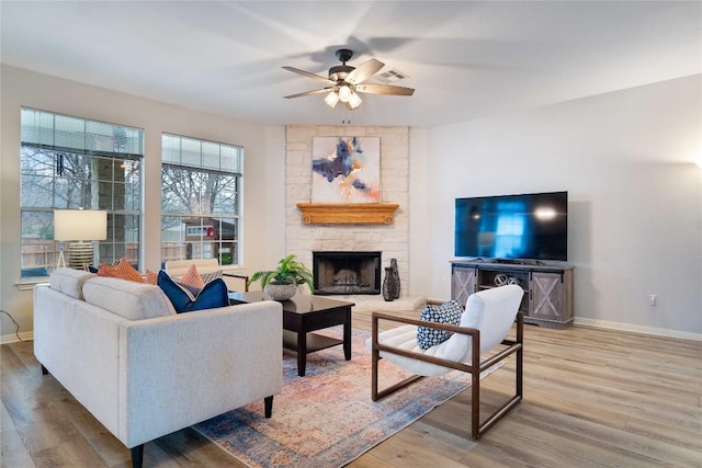 living room with visible vents, baseboards, a ceiling fan, wood finished floors, and a stone fireplace