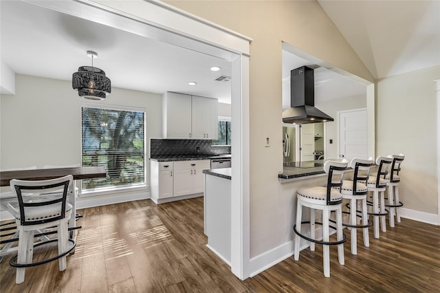 kitchen featuring exhaust hood, decorative backsplash, white cabinets, decorative light fixtures, and vaulted ceiling