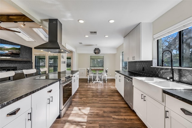 kitchen with appliances with stainless steel finishes, decorative backsplash, island range hood, white cabinets, and dark hardwood / wood-style flooring