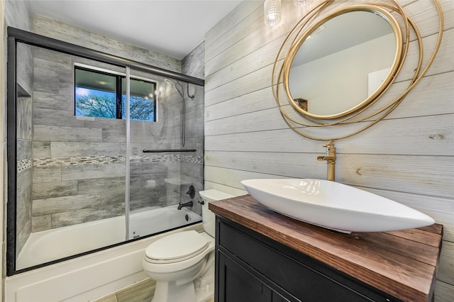 full bathroom with wooden walls, toilet, enclosed tub / shower combo, and vanity