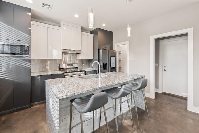 kitchen with sink, white cabinets, decorative light fixtures, stainless steel appliances, and a center island with sink