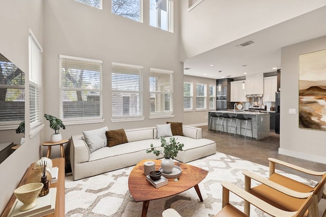 living area featuring baseboards, a high ceiling, and visible vents