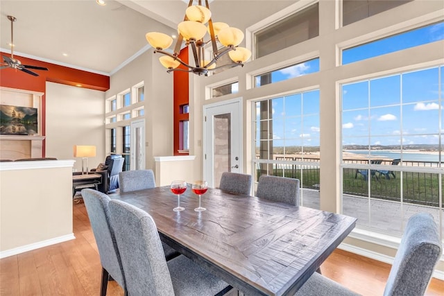 dining space with a high ceiling, ornamental molding, light wood-style floors, a chandelier, and ceiling fan