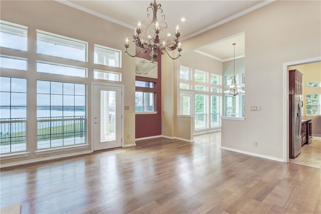 unfurnished living room with a chandelier, baseboards, light wood-style flooring, a towering ceiling, and ornamental molding