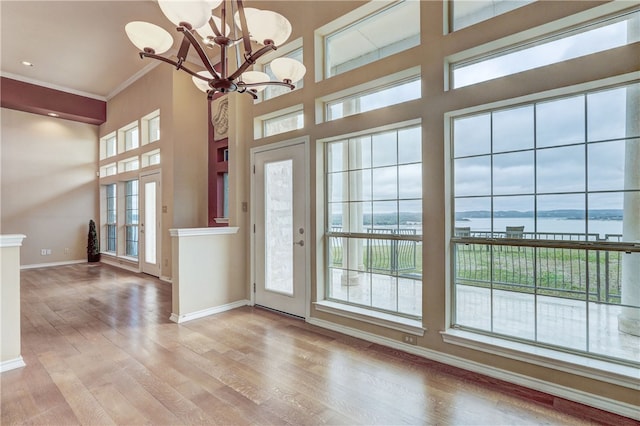 foyer entrance with a chandelier, baseboards, a water view, wood finished floors, and crown molding