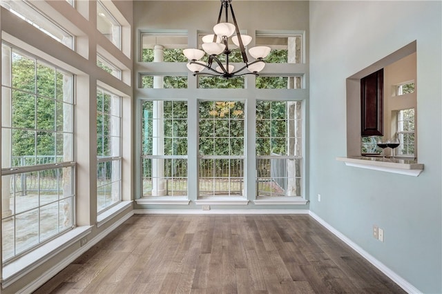 unfurnished dining area with baseboards, a towering ceiling, wood finished floors, and a chandelier
