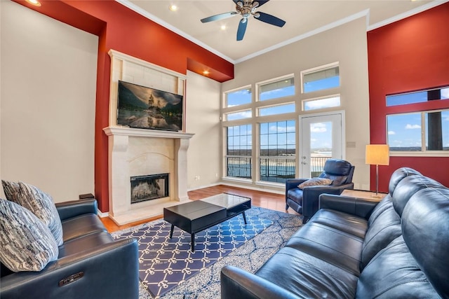 living room featuring a ceiling fan, wood finished floors, a high end fireplace, ornamental molding, and plenty of natural light