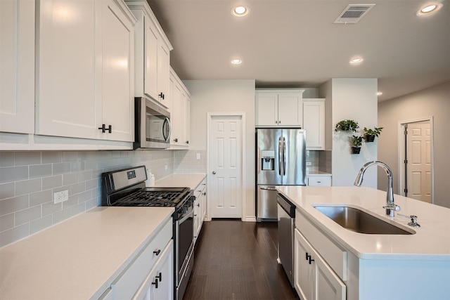 kitchen with white cabinets, stainless steel appliances, sink, backsplash, and a kitchen island with sink