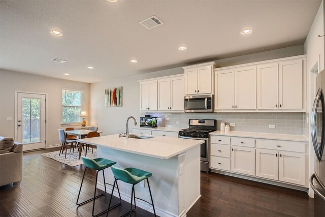 kitchen featuring appliances with stainless steel finishes, tasteful backsplash, white cabinetry, sink, and an island with sink