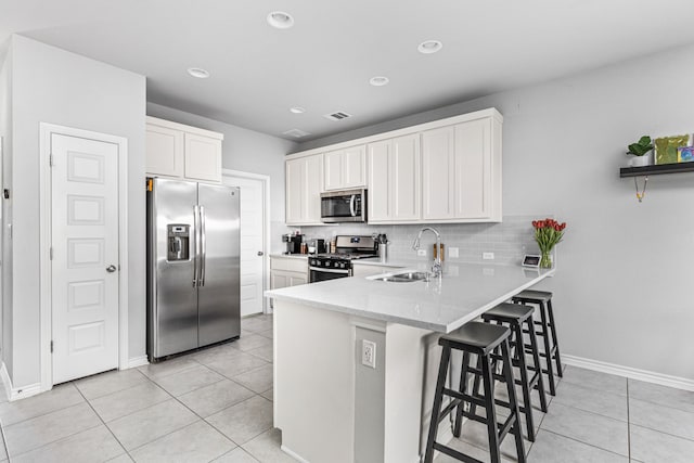 kitchen with a kitchen breakfast bar, appliances with stainless steel finishes, sink, white cabinetry, and light tile patterned floors