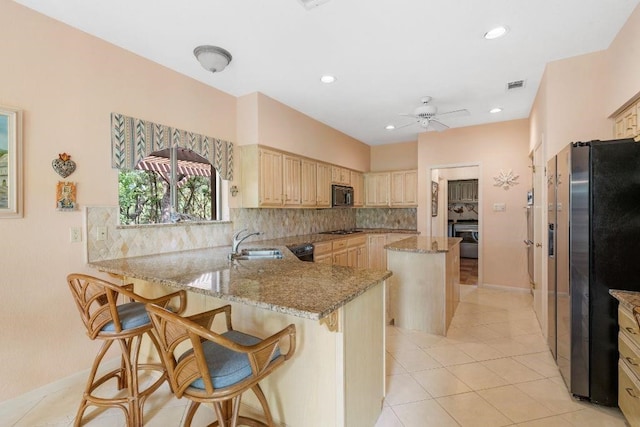 kitchen featuring black appliances, sink, kitchen peninsula, light stone counters, and a breakfast bar