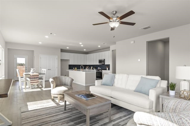 living room with ceiling fan, light hardwood / wood-style floors, and sink