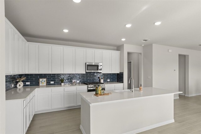 kitchen featuring sink, white cabinets, decorative backsplash, stainless steel appliances, and a center island with sink