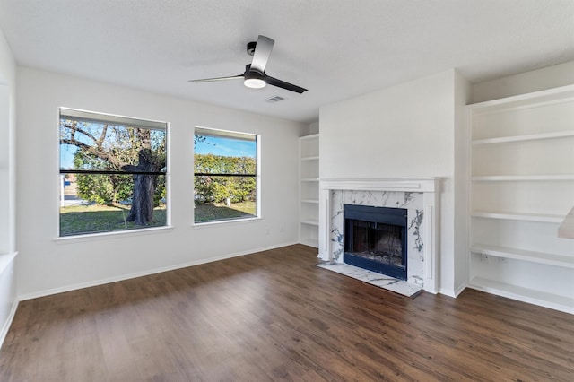 unfurnished living room featuring a premium fireplace, ceiling fan, built in shelves, and dark hardwood / wood-style floors