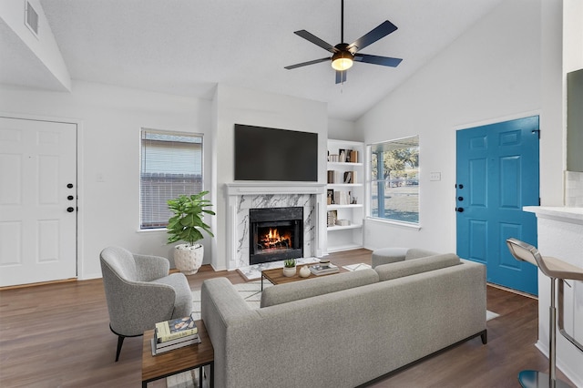 living room with ceiling fan, high vaulted ceiling, a high end fireplace, and dark wood-type flooring