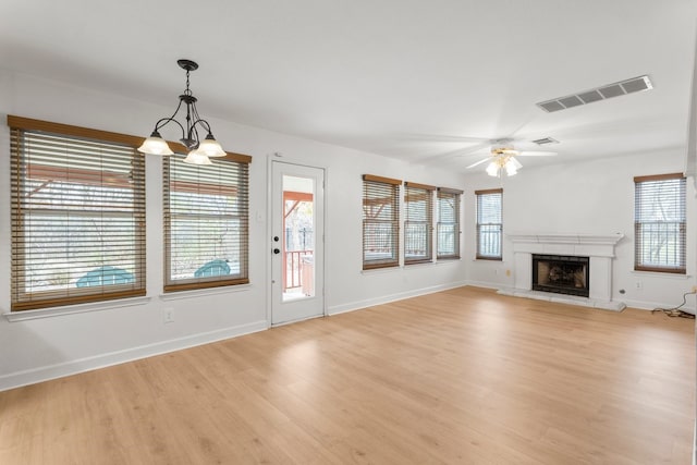 unfurnished living room with a high end fireplace, light hardwood / wood-style floors, and ceiling fan with notable chandelier