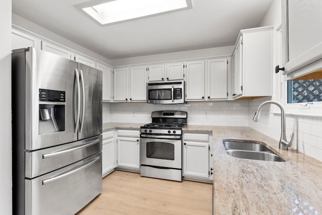 kitchen with stainless steel appliances, light stone counters, white cabinets, decorative backsplash, and sink