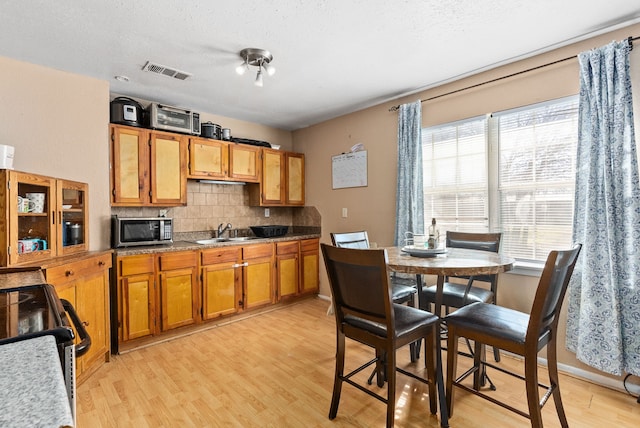 kitchen with light hardwood / wood-style floors, a textured ceiling, range, decorative backsplash, and sink