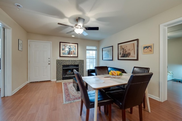 dining area featuring a tiled fireplace, light hardwood / wood-style floors, and ceiling fan