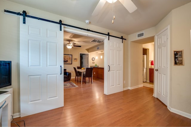 living room with ceiling fan, a barn door, and light hardwood / wood-style flooring