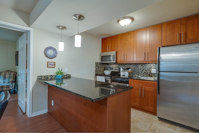 kitchen featuring kitchen peninsula, appliances with stainless steel finishes, sink, decorative light fixtures, and decorative backsplash