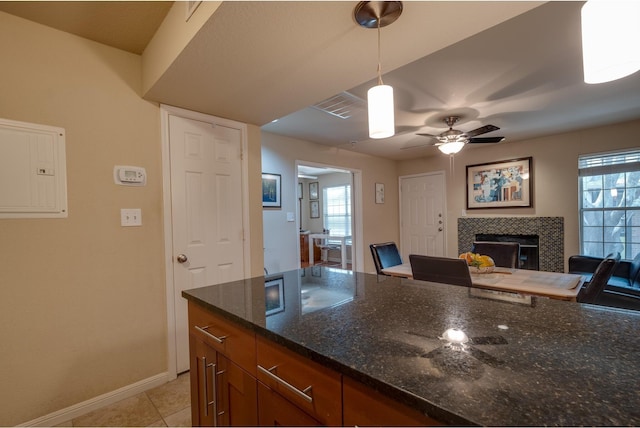 kitchen with electric panel, decorative light fixtures, dark stone countertops, a fireplace, and light tile patterned floors