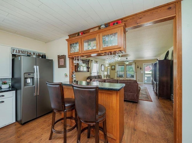 kitchen featuring hardwood / wood-style flooring, stainless steel refrigerator with ice dispenser, white cabinets, kitchen peninsula, and a breakfast bar