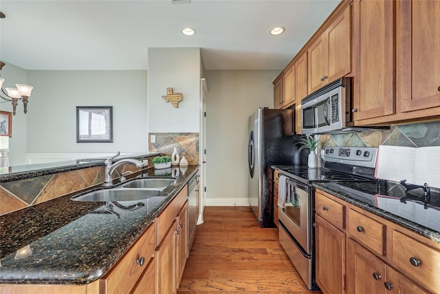 kitchen featuring appliances with stainless steel finishes, hardwood / wood-style flooring, sink, dark stone countertops, and pendant lighting