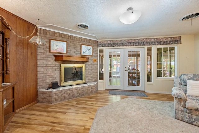 living room with a textured ceiling, french doors, a fireplace, light hardwood / wood-style floors, and ornamental molding