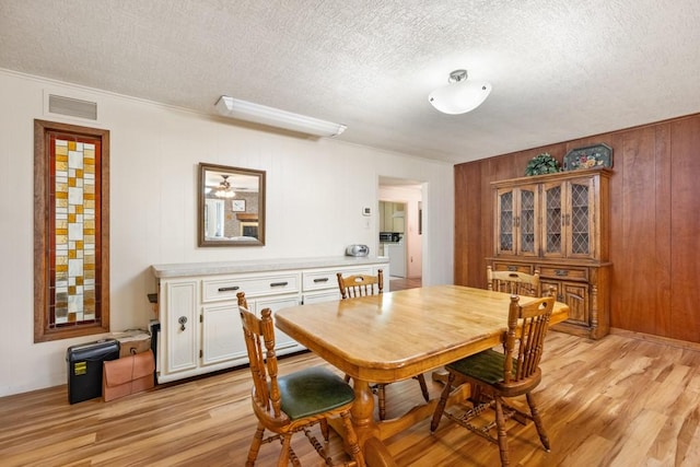 dining room featuring a textured ceiling, crown molding, wood walls, and light wood-type flooring