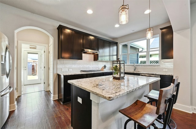 kitchen featuring appliances with stainless steel finishes, hanging light fixtures, a kitchen island, light stone counters, and dark hardwood / wood-style floors